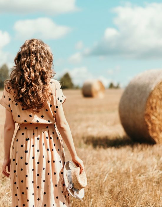 Young woman standing on harvested field with straw bales. Agriculture background with copy space